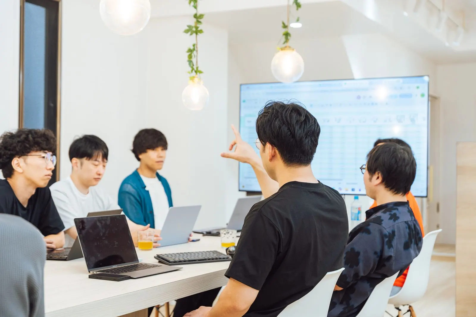 大きな画面を前に、身ぶりを交えて話し合うメンバーたち